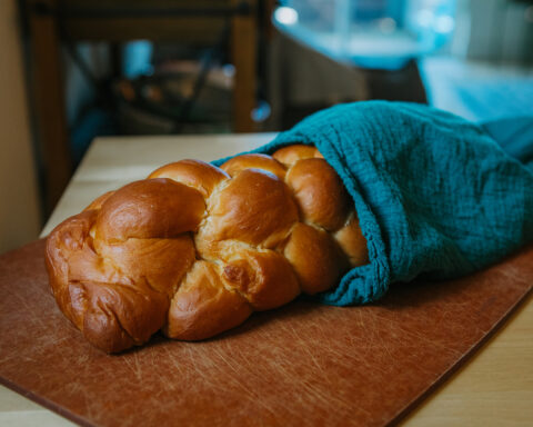 a loaf of challah wrapped in a blue towel rests on cutting board