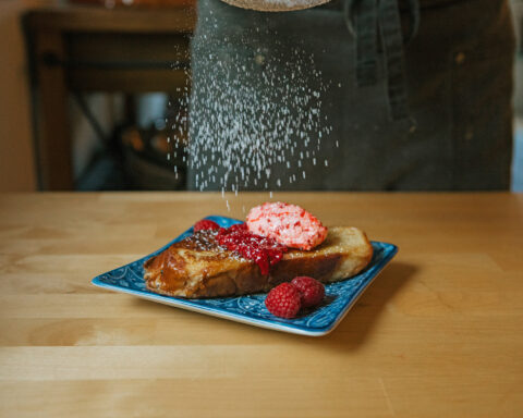 french toast with berries atop a blue plate with powdered sugar being sprinkled on top