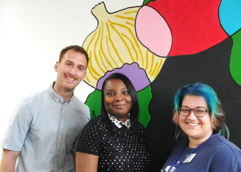 Matt, Freda, and Meg are in front of a food mural that was painted by kids at the Community Center. 