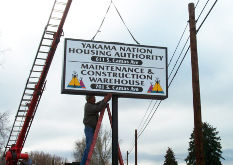 person stands on ladder under Yakama Nation Housing Authority sign.